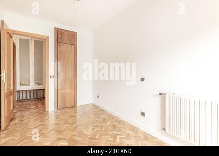 Camera vuota con piccolo armadio in rovere da incasso con radiatore in alluminio bianco e pavimenti in parquet di rovere chiaro a spina di pesce Foto Stock