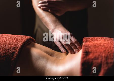 Massaggio professionale della schiena e della parte inferiore della schiena. Massaggiatore maschile massaggia un cliente a una donna in una stanza buia a lume di candela Foto Stock