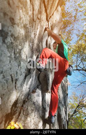 Un uomo bearded invecchiato con un sacchetto di magnesia e scarpe di roccia è addestrato su una roccia non alta nei boschi. Formazione di scalatori in n Foto Stock