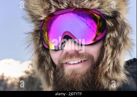 Primo piano ritratto di un felice sciatore bearded snowboarder in una maschera da sci con occhiali e un grande cappello di pelliccia vecchia scuola su sfondo o Foto Stock