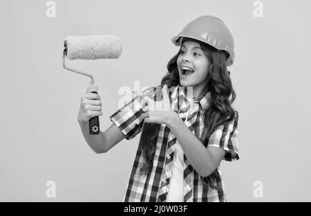 felice ragazza teen con capelli ricci in costruzione casco puntando dito su rullo vernice, rinnovare Foto Stock