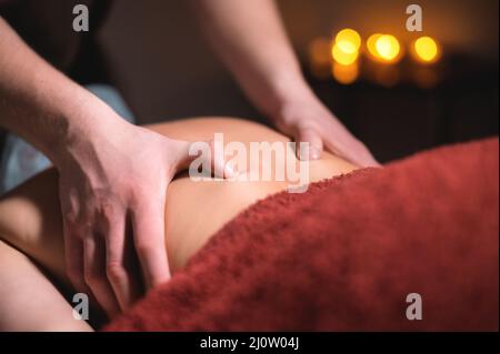 Massaggio professionale della schiena e della parte inferiore della schiena. Massaggiatore maschile massaggia un cliente a una donna in una stanza buia a lume di candela Foto Stock