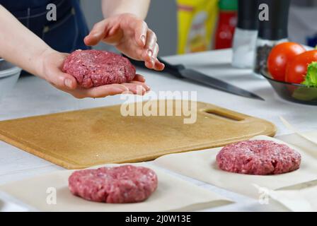 Mano della donna che forma una carne di manzo per una festa di hamburger. Porzionamento carne macinata. Hamburger fatti in casa. Fare il cibo a casa. Foto Stock