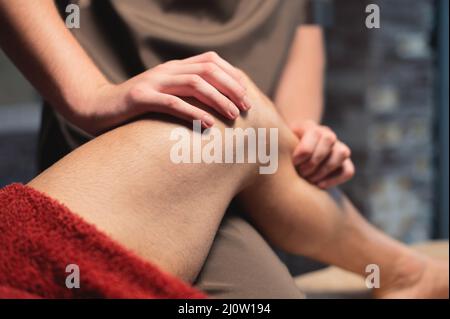 Un massaggiatore maschile massaggia il muscolo del vitello a un atleta maschile in un salone di massaggi professionale. Massaggio sportivo nel 4K Foto Stock