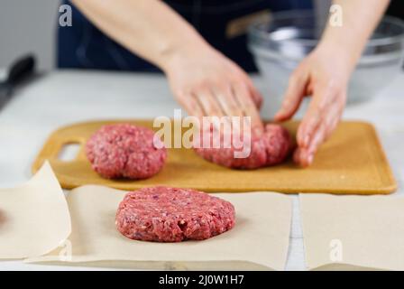 Mano della donna che forma una carne di manzo per una festa di hamburger. Porzionamento carne macinata. Hamburger fatti in casa. Fare il cibo a casa. Foto Stock