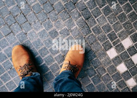 Piedi uomo in stivali marroni e jeans blu si levano in piedi sul ciottoli. Primo piano Foto Stock