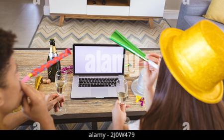 Giovane coppia biraciale che soffia corna durante le videochiamate su un computer portatile con schermo vuoto e spazio per la copia Foto Stock