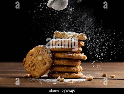 Pila di biscotti rotondi al forno cosparsi di zucchero in polvere su un tavolo di legno, sfondo nero Foto Stock