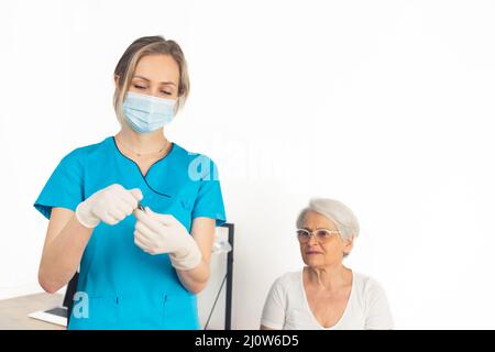 Il medico in uniforme blu prepara un vaccino per la sua paziente anziana signora pensionata. Foto di alta qualità Foto Stock