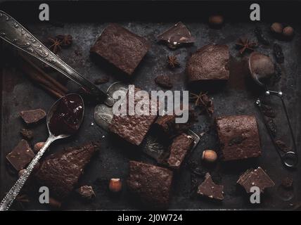 Pezzi di torta brownie al cioccolato al forno in un foglio di metallo da forno su un tavolo nero Foto Stock