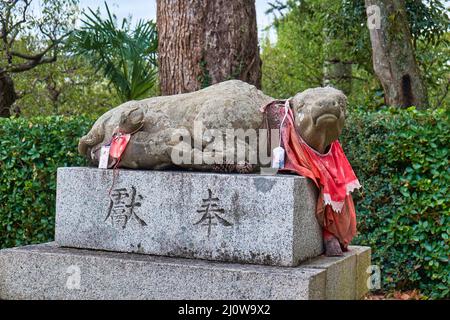 La statua in pietra del bue sdraiato nel bib rosso al santuario di Kitano Tenmangu. Kyoto. Giappone Foto Stock