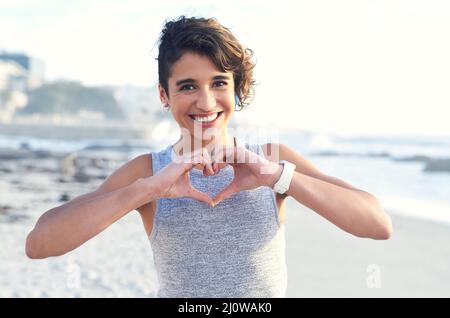 Condividere un po 'd'amore estate. Scatto corto di una donna che forma un cuore forma con le sue mani alla spiaggia. Foto Stock