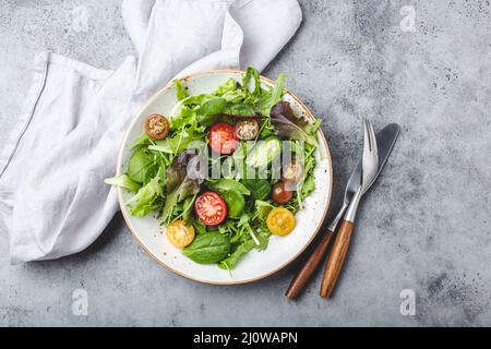 Verdure insalata sana con pomodori ciliegini rossi e gialli, pepe e foglie di insalata verde su piatto bianco rustico in ceramica Foto Stock