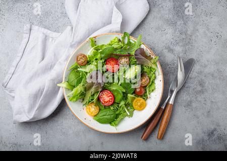 Verdure insalata sana con pomodori ciliegini rossi e gialli, pepe e foglie di insalata verde su piatto bianco rustico in ceramica Foto Stock