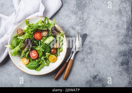 Verdure insalata sana con pomodori ciliegini rossi e gialli, pepe e foglie di insalata verde su piatto bianco rustico in ceramica Foto Stock