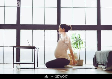 Tutta la lunghezza di giovane calma donna incinta che fa yoga in linea a casa Foto Stock