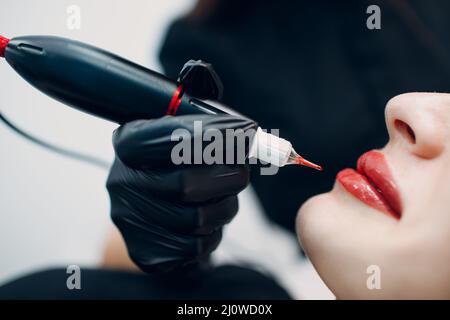 Cosmetologo applicazione rosso permanente compongono tatuaggio sulle labbra della giovane donna Foto Stock