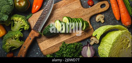 Cetriolo tritato su tagliere di legno con coltello e verdure fresche assortite Foto Stock