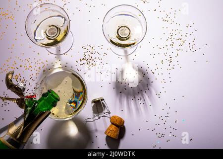 Vista dall'alto di una bottiglia di champagne in bicchiere su confetti su sfondo bianco Foto Stock