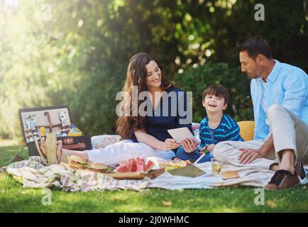 Pranzare all'aperto è fantastico. Scatto di una giovane famiglia utilizzando un tablet digitale durante un picnic nel parco. Foto Stock