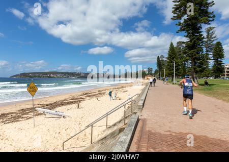 L'uomo si esercita facendo jogging lungo il lungomare di fronte alla spiaggia di Manly Beach a Sydney, Australia, la spiaggia è chiusa a causa delle inondazioni Foto Stock