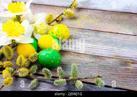 Composizione pasquale di fiori di narciso, rametti di salice fioriti e uova pasquali con un modello di fiori gialli e verdi su un Foto Stock