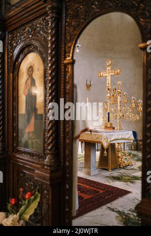 Candelabro d'oro su un tavolo di fronte a una croce nella Chiesa di San Sava in Tivat. Vista attraverso l'arco Foto Stock