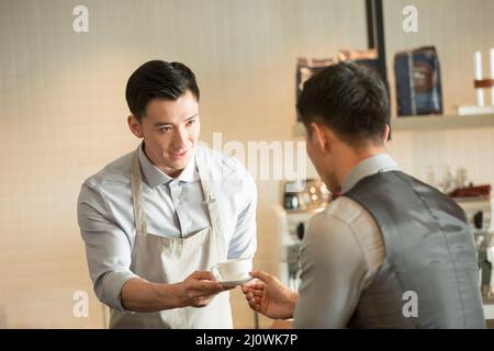 Il cameriere giovane offre all'uomo d'affari una tazza di caffè Foto Stock