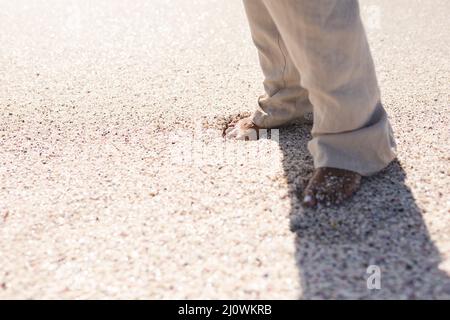 Sezione bassa di donna biraciale anziana in piedi nudi sulla sabbia in spiaggia durante la giornata di sole Foto Stock