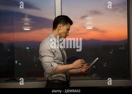 Un uomo d'affari cinese di successo che lavora con un tablet digitale in ufficio Foto Stock