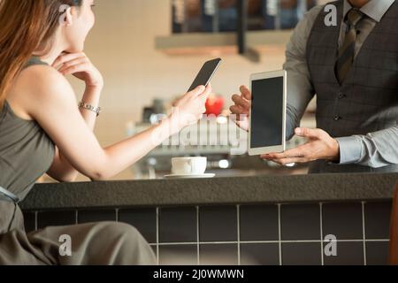 Primo piano della giovane donna cinese paga un cameriere con il suo cellulare in caffè Foto Stock