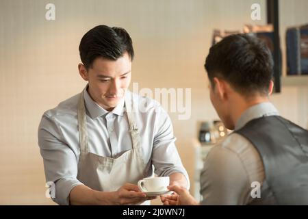 Il primo piano del cameriere giovane offre all'uomo d'affari una tazza di caffè Foto Stock