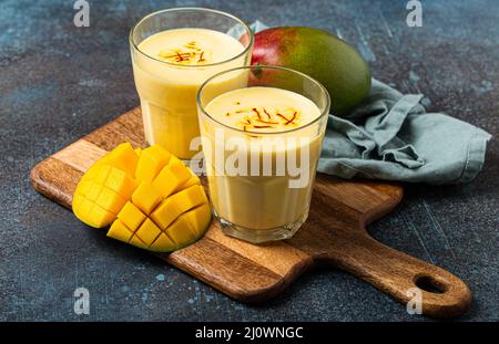 Bevete mango lassi in due bicchieri su tavola rustica in cemento con manfo fresco tagliato maturo dall'alto Foto Stock