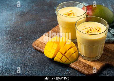 Bevete mango lassi in due bicchieri su tavola rustica in cemento con manfo fresco tagliato maturo dall'alto Foto Stock
