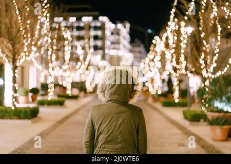 Una ragazza in un cappuccio con pelliccia si trova su una strada decorata per Natale in città. Foto Stock