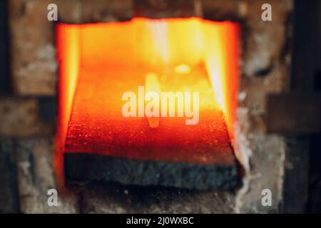 Blacksmith forge oven with hot flame. Smith heating iron piece of steel in fire of red-hot forge Stock Photo