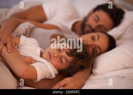 Vuole sempre essere vicino a mummia e papà. Scatto corto di una giovane famiglia a letto insieme. Foto Stock