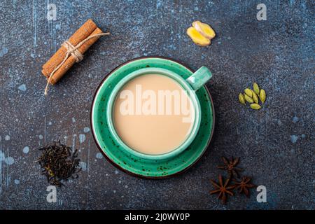 Tè indiano bevanda calda con latte e spezie in rustico verde teacup con ingredienti per la preparazione di masala chai Foto Stock
