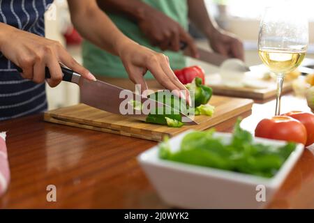 Metà della giovane donna biraciale tagliando peperone in cucina a casa Foto Stock