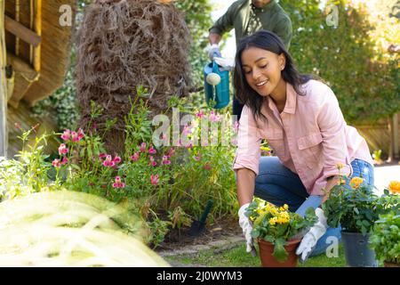 Sorridendo giovane afroamericana che pianta i fiori mentre giardinaggio al cortile Foto Stock