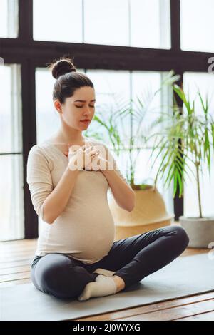 Meditazione durante la gravidanza. Giovane donna incinta calma e tranquilla che fa yoga a casa Foto Stock