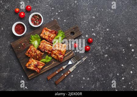 Costolette di maiale cotte alla griglia con spezie e verdure su tagliere di legno su sfondo scuro. Concetto di cibo americano. Vista dall'alto, Foto Stock