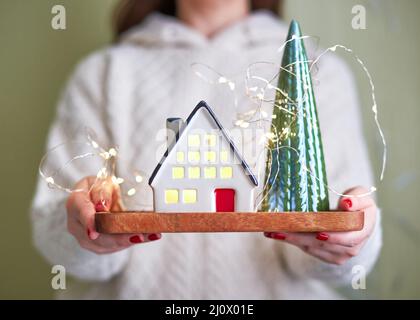 La donna tiene in mano la casa in ceramica con la luce all'interno. Il concetto di vacanza, natale e coziness Foto Stock