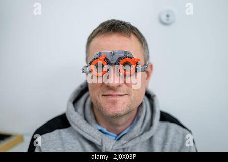 Correzione della visione. Selezione di occhiali. Montature di prova professionali sul viso del paziente maschile mentre il medico controlla la vista in MODER Foto Stock