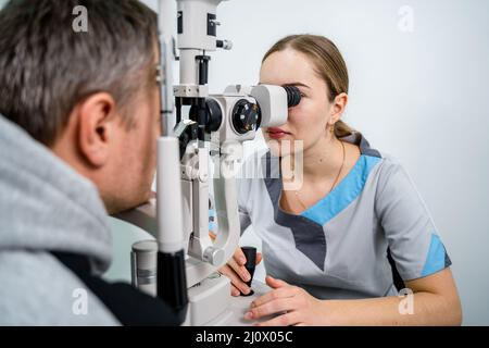Optometristo che esamina gli occhi di un paziente di sesso maschile in una moderna clinica oftalmologica. Medico oculare con paziente umano durante un esame Foto Stock