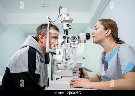 Oftalmologo e esame della vista da parte del paziente. Uomo che fa il test dell'occhio con optometrist. Oftalmologo che utilizza un apparecchio per esami oculari Foto Stock