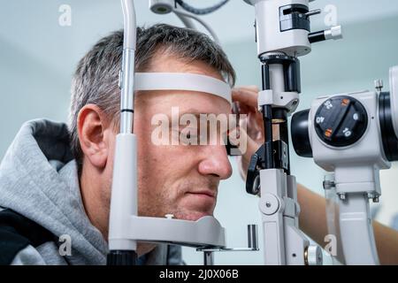 Optometristo che esamina gli occhi di un paziente di sesso maschile in una moderna clinica oftalmologica. Medico oculare con paziente umano durante un esame Foto Stock