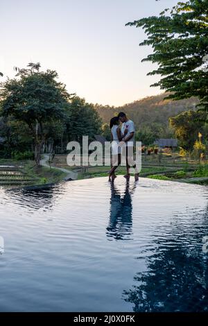 Coppia uomo e donna guardando il tramonto su un bordo di una piscina con una vista sulle montagne e risaie del nord Thailandia ma Foto Stock