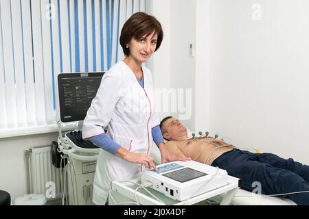 ECG concept. Woman doctor cardiologist doing electrocardiogram test to man patient in cardiology clinic. Medicine, cardiology, E Stock Photo