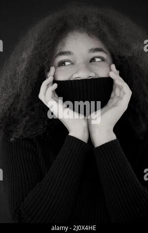 Pleased african american curly woman with closed eyes covering face with warm black sweater collar Stock Photo